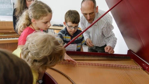 Instrumentenzug Cembalo Eine Mann zeigt einer Gruppe Kindern ein offenes Cembalo