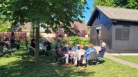 Eine Gruppe Menschen beim Picknick unter Bäumen vor einer Holzkirche