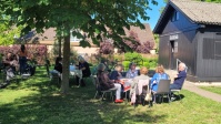 Eine Gruppe Menschen beim Picknick unter Bäumen vor einer Holzkirche