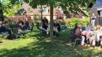 Eine Gruppe von Menschen beim Picknick im Garten vor einer Holzkirche